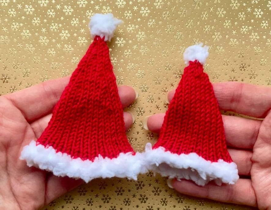 Hands holding the 2 knitted Barbie Santa hat sizes for scale - oversized on the left, fitted on the right