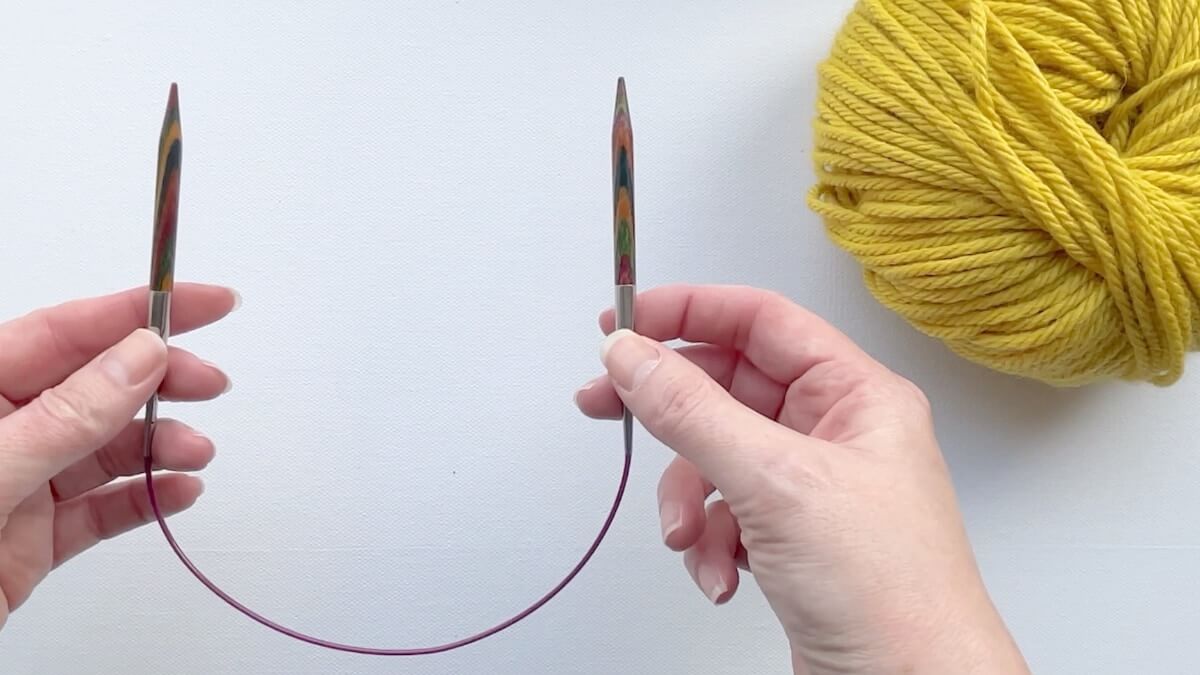 16 inch circular needle with 6mm tips in hands beside chunky yellow wool