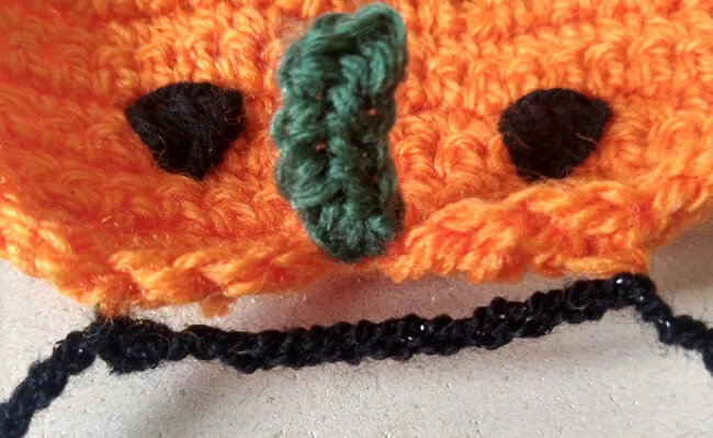 Close up showing the black garland string attached near the top back of the pumpkin at each edge with chains made in between.