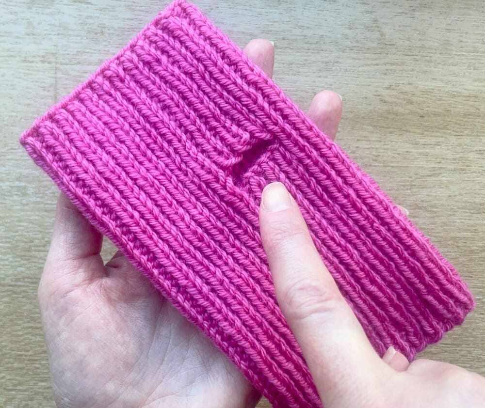 Finger pointing at thumb hole made by casting off stitches at start of 1 round and casting on stitches at the start of the next round