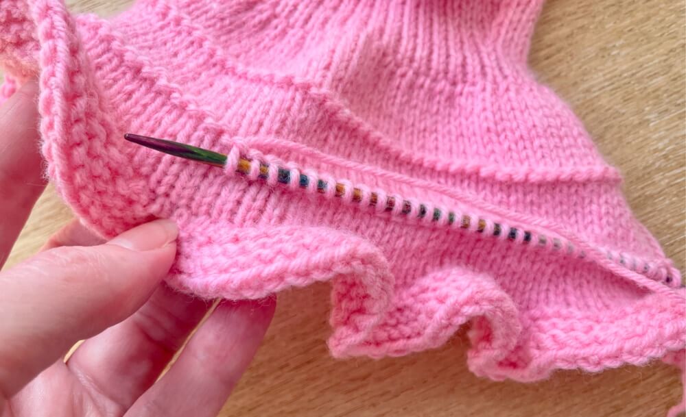 Put your needle through the n shape in each purl stitch to pick up and knit a stitch