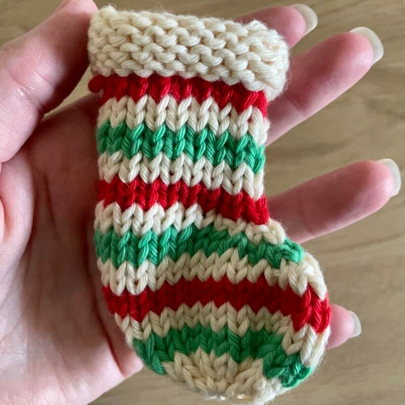 Close up of hand holding mini knitted striped Christmas stocking decoration